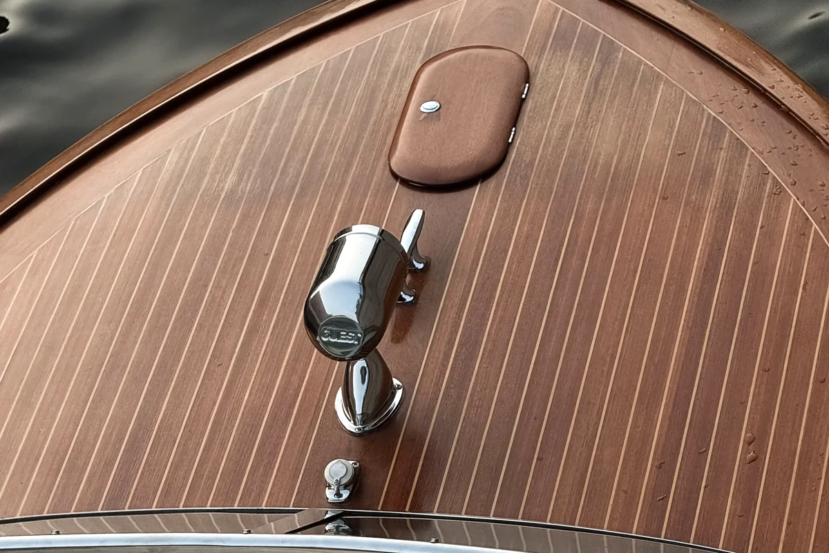 Top view of a classic boat bow with warm deck lines, a hatch, and chrome hardware.